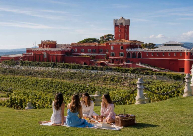 Four friends enjoying a picnic on the grounds of Château de Crémat with a Provençal basket and castle views — Girls' Trip with High Point Holidays.